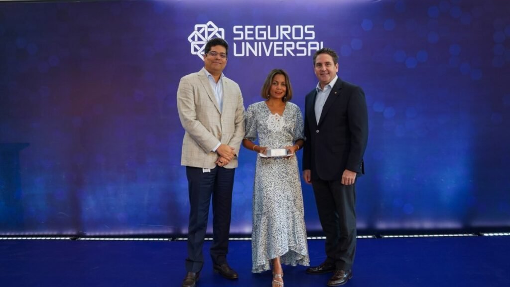 Seguros Universal se consolida liderazgo con 21% del mercado Rafael E. Izquierdo y el vicepresidente ejecutivo senior de Filiales de Seguros de Grupo Universal, Wilfredo Baquero Ginebra, entregan un reconocimiento a Angelika Charlotte Wolff.